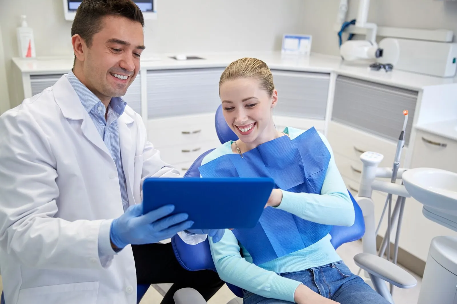 Dentista de jaleco branco mostra um tablet a uma paciente sorridente sentada na cadeira do consultório